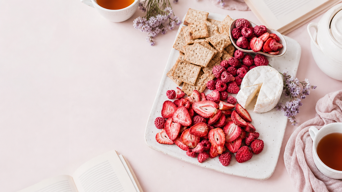 An airy book club snack board with freeze-dried strawberries, raspberries, crackers, soft cheese, and open books on a blush table