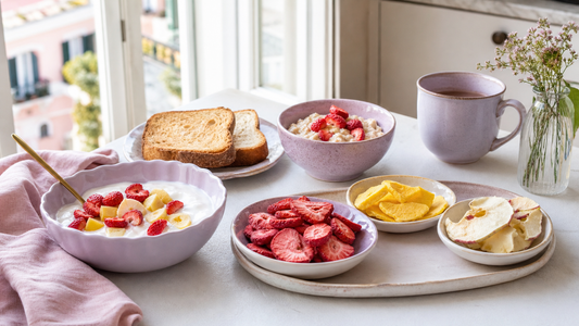 Airy vacation rental breakfast table with pastel bowls of yogurt, toast, peaches, and freeze-dried strawberries and mango in soft morning light
