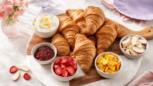 Buttery croissant brunch board with whipped ricotta berry jam and bowls of colorful freeze-dried fruit on a blush table