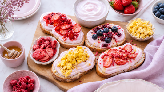 Brunch board with pink yogurt toast slices topped with freeze-dried strawberries, mango, berries, and honey on a soft pink table setting