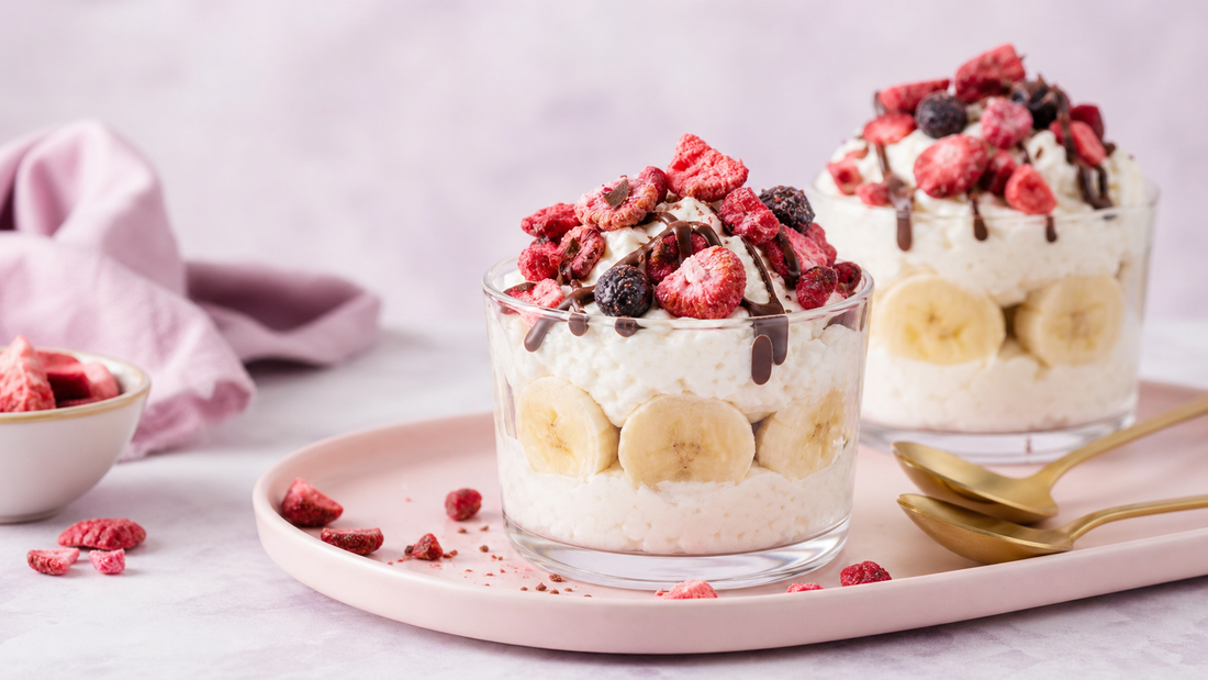 Pastel dessert scene with glass cups filled with whipped cottage cheese and banana slices, topped with freeze-dried strawberries, dark chocolate drizzle, and soft pink lavender styling