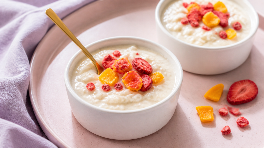 Two white ceramic cups of creamy rice pudding topped with freeze-dried strawberries and mango on a blush brunch tray