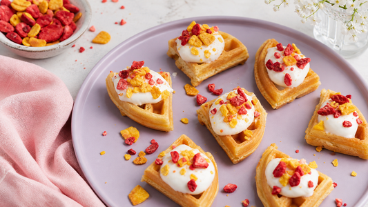Mini waffle bites topped with yogurt and freeze-dried fruit on a soft pink breakfast board for How to Make Mini Yogurt Waffle Bites with Freeze-Dried Fruit