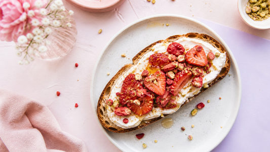 A thick slice of labneh toast topped with freeze-dried strawberries on a blush brunch plate with airy white and pale lavender styling