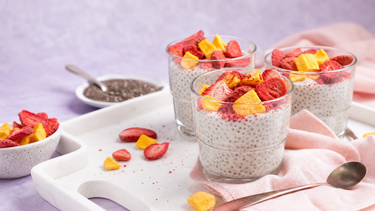 Vanilla chia pudding cups topped with freeze-dried strawberries and mango on a white tray with blush and lavender styling