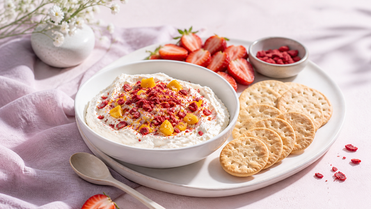 Soft pink snack board with a bowl of whipped cottage cheese dip topped with freeze-dried strawberries, fruit pieces, and crackers in natural light