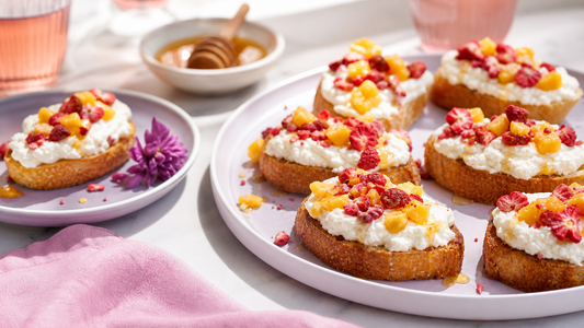 Whipped ricotta crostini topped with freeze-dried strawberries and mango on pale lavender plates in a bright brunch scene