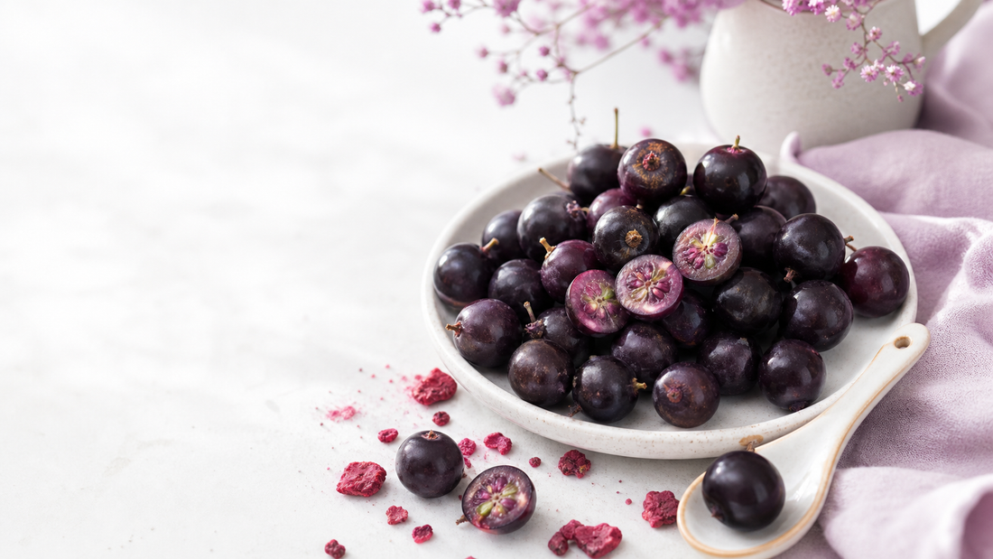White plate of deep purple jostaberries with a few berries cut open, bright berry crumbs, pale lavender linen, and airy natural light
