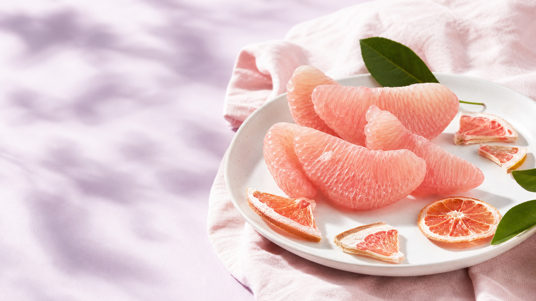Pomelo wedges on a white plate with pale pink linen and soft lavender backdrop