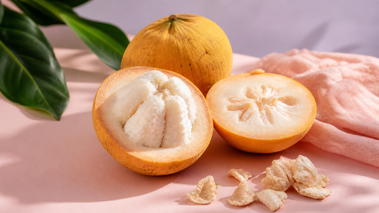 Cut santol fruit on a blush pink surface with creamy white flesh visible in a soft editorial tropical fruit scene